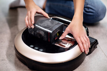 Woman cleans dust from robot vacuum cleaner