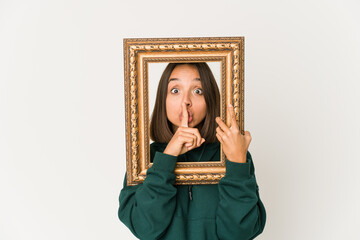 Young hispanic woman holding an old frame keeping a secret or asking for silence.