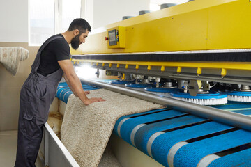 Man operating carpet automatic washing machine in professional laundry service