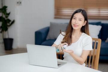 Young asian woman work from home with alcohol gel or sanitizer for cleaning hand and protect coronavirus or covid-19, new normal, quarantine and social distancing, businesswoman using laptop computer.