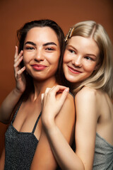 two pretty diverse girls happy posing together: blond and brunette on brown background, lifestyle people concept