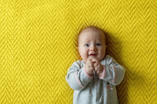 Happy caucasian baby girl four months old lying on knitted blanket. Colors of the year 2021 ultimate gray and illuminating