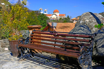 a picturesque picture of a bench for rest against the background of a church in the mountains of cyprus