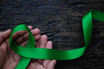 Top view of hands holding green color ribbon on dark background. Gall bladder and bile duct cancer,...