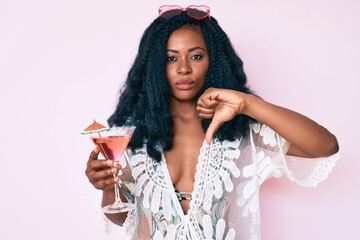 Beautiful african woman wearing summer look and drinking cocktail with angry face, negative sign showing dislike with thumbs down, rejection concept