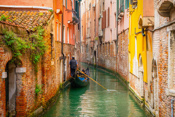Venetian gondolier punting gondola through green canal waters of Venice Italy