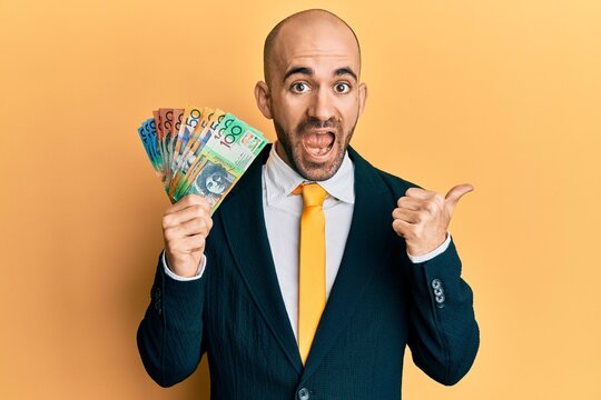 Young hispanic business man holding canadian dollars pointing thumb up to the side smiling happy with open mouth
