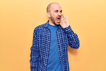 Young handsome bald man wearing casual shirt shouting and screaming loud to side with hand on mouth. communication concept.