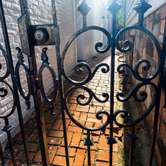An abstract image of a narrow passageway behind locked gate. The stylish metal railings and the brick floor gives a mysterious look that is out of reach. Sunshine penetrates through the top