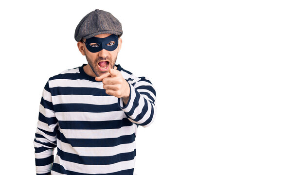 Young handsome man wearing burglar mask pointing displeased and frustrated to the camera, angry and furious with you