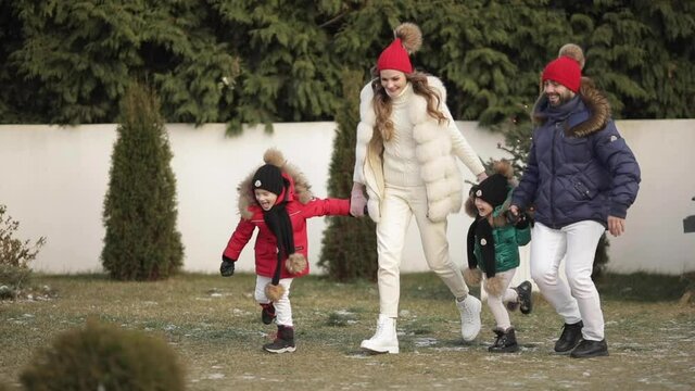 Xmas family holidays, young parents with kids holding hands running joyfully outdoor near christmas tree and home. High quality HD footage