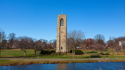 Baker Park, a city park by Carrol Creek with large open meadows, trees, walking and cycling paths and the famous historic  tower and carillon. Image shows Frederick cityscape with the river.