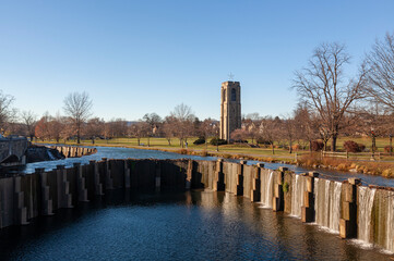 Fototapeta na wymiar Baker Park, a city park by Carrol Creek with large open meadows, trees, walking and cycling paths and the famous historic tower and carillon. Image shows Carrol Creek with waterfalls and the park
