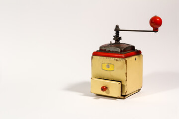 Old wooden colored manual coffee grinder with red handle, on white background.