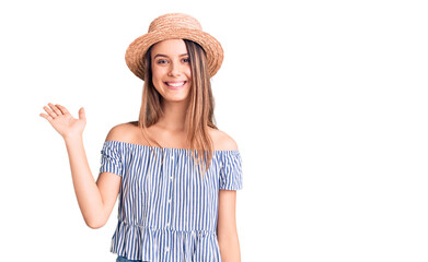 Young beautiful girl wearing hat and t shirt smiling cheerful presenting and pointing with palm of hand looking at the camera.