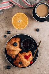 Croissants with fresh berries, orange and jam with cup of coffee on a concrete background.