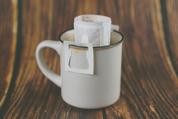Instant drip coffee with paper dripping bag in a mug on wooden table