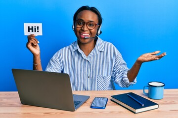 Young african woman wearing operator headset holding hi word celebrating achievement with happy smile and winner expression with raised hand