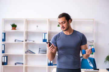 Young handsome employee doing sport exercises in the office