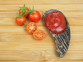ketchup or tomato sauce in wooden spoon and fresh tomatoes on wooden background.