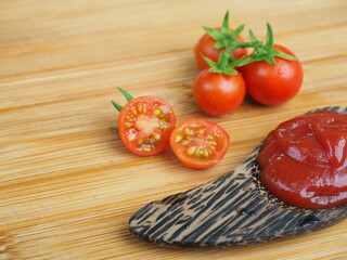 ketchup or tomato sauce in wooden spoon and fresh tomatoes on wooden background.