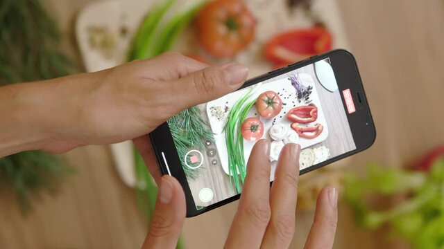 Food blogger woman hands shoots video of board with vegetables on wooden table. Food photo. Vegan blogging lunch. Close up. Slow motion