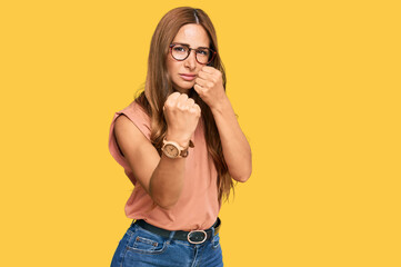 Young hispanic woman wearing casual clothes and glasses ready to fight with fist defense gesture, angry and upset face, afraid of problem