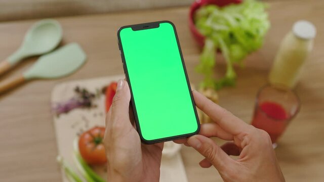Close up hands woman hold phone with vertical green screen on vegetables on wooden tablet background. Health food kitchen. Vegan blogging lunch blogger. Slow motion