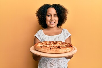 Young little girl with afro hair holding italian pizza winking looking at the camera with sexy...