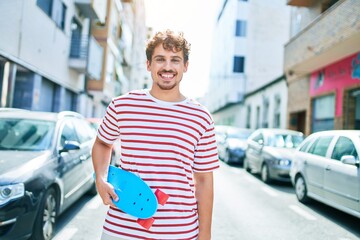 Young caucasian skater man smiling happy holding skate walking at street of city. © Krakenimages.com