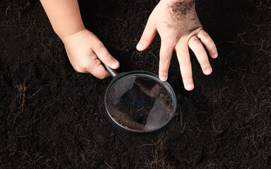 Top view of child hand hold magnifying glass for check black soil at the garden, Concept of global pollution, Save Earth and World Soil Day