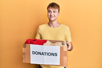 Young caucasian man holding donations box for charity smiling looking to the side and staring away thinking.