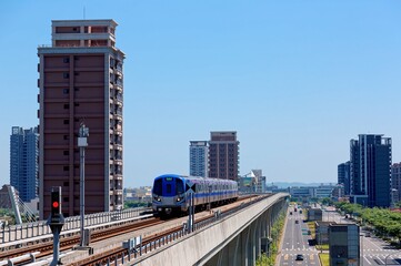 Obraz na płótnie Canvas Scenic view of a metro train traveling on elevated rails of Taoyuan Mass Rapid Transit System (Taoyuan International Airport MRT System) under sunny blue sky in Chunli, New Taipei City, Taiwan