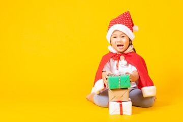 Asian little cute child girl smile face, a kid dressed in red Santa Claus hat the concept of holiday Christmas Xmas day or Happy new year, isolated sitting on yellow background