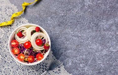 Top view of the healthy colorful salad bowl with tomatoes fresh mixed greens vegetable in a dish and measuring tape on cement background, Health salad snack diet food weight loss concept