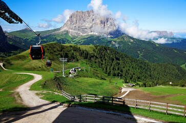 Summer scenery of rocky Mountains Sassolungo (Langkofel) & Schlern (Sciliar) under sunny sky with cable cars & country roads going up and down the valley in Dantercepies, Selva di Val Gardena, Italy 