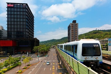 Obraz premium Scenic view of a train traveling on elevated rails of Taipei Metro System ( Taipei Mass Rapid Transit ) between residential towers in suburban area under blue sunny sky