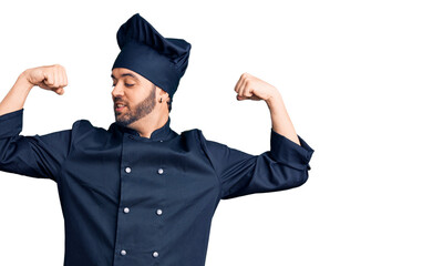 Young hispanic man wearing cooker uniform showing arms muscles smiling proud. fitness concept.