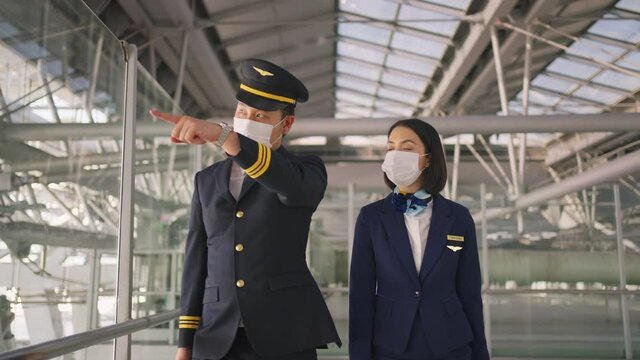 Asian pilot and flight attendant talking while walking in the airport.