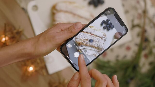 Young hands woman hold phone with vertical shoots video of tasty dessert. Christmas time. Blogger blogging cuisine dish. Slow motion