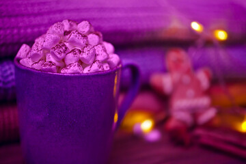 Cocoa drink with marshmallows in a blue cup, sweet spices, gingerbread man and a stack of knits on a wooden background.