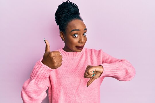 Young african american woman wearing casual winter sweater doing thumbs up and down, disagreement and agreement expression. crazy conflict