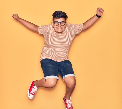 Adorable kid wearing casual clothes and glasses smiling happy. Jumping with smile on face and arms opened over isolated yellow background