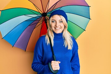 Young caucasian woman holding colorful umbrella smiling with a happy and cool smile on face. showing teeth.