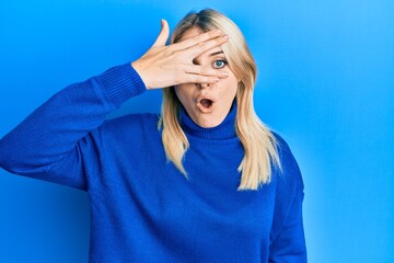 Young caucasian woman wearing casual winter sweater peeking in shock covering face and eyes with...