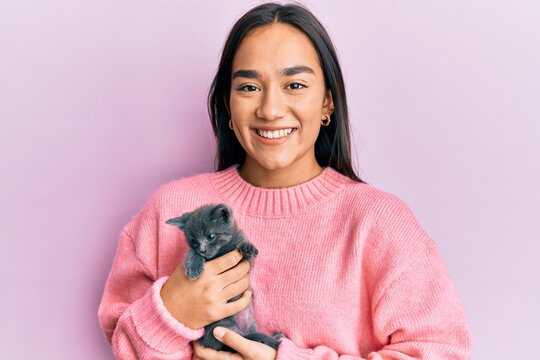 Young hispanic girl smiling happy holding cute cat over isolated pink background.