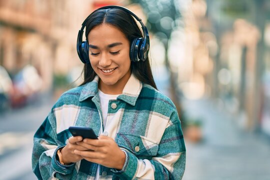Young latin girl smiling happy using smartphone and headphones at the city.