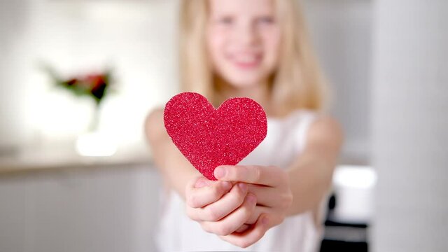 Red heart close up in hands of little blonde smiling girl on Valentines Day. Slow motion