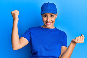 Beautiful brunette woman wearing delivery uniform screaming proud, celebrating victory and success very excited with raised arms