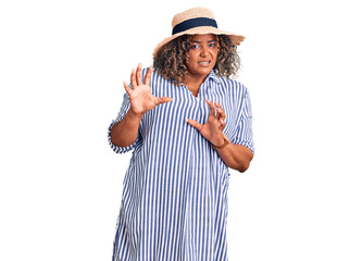 Young african american plus size woman wearing summer hat disgusted expression, displeased and fearful doing disgust face because aversion reaction. with hands raised